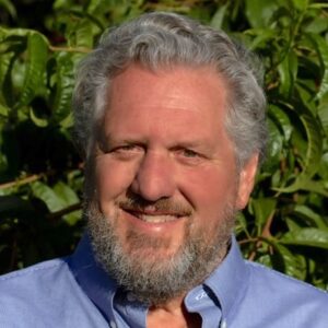 Smiling man with white hair and beard against bushes